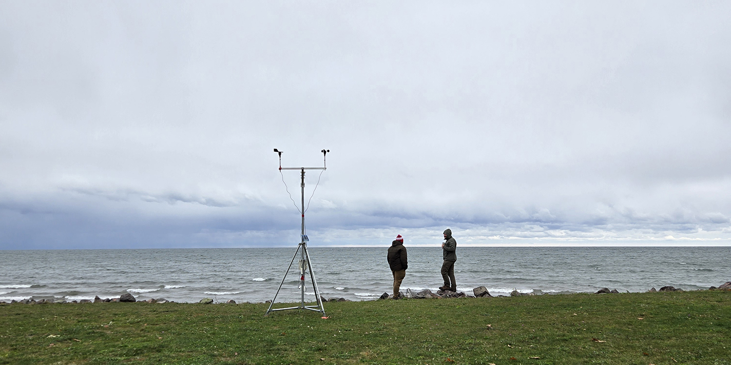 Two people stand on a lake shore next to a measuring device